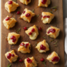 Delicious golden cranberry brie bites on a wooden board, garnished with rosemary, ready to serve as a holiday appetizer.