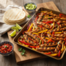 Overhead view of sizzling, colorful sheet pan chicken fajitas with charred chicken and vegetables, served on a rustic board w